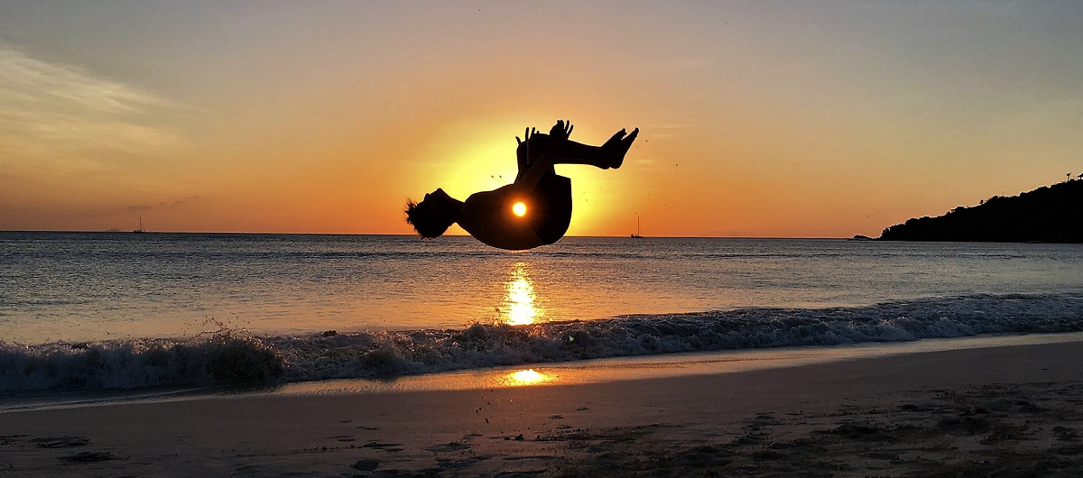 Athlete performing a somersault on a beach at sunset after recovering from a leg fracture with Fit Again Sports Therapy.